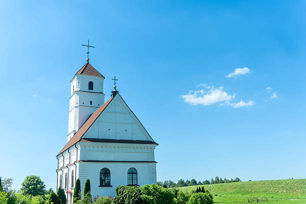Peaceful white church with red tiled roof and bell tower under blue sky. Transfiguration church in Zaslavl Belarus with white walls and red roof.