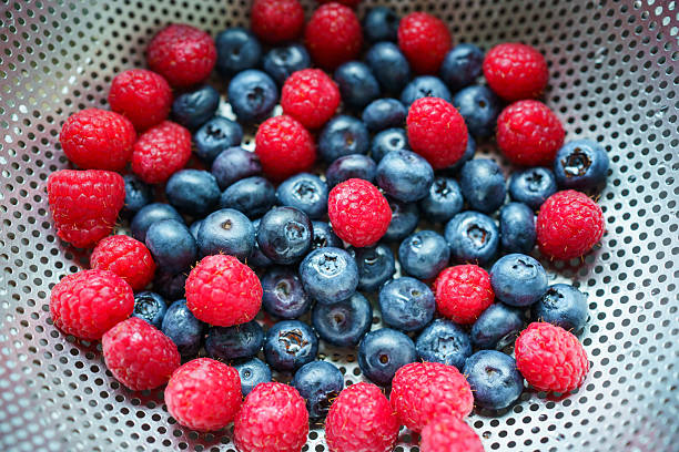 fresh blueberries and raspberries in a bowl on white table, vertical top view