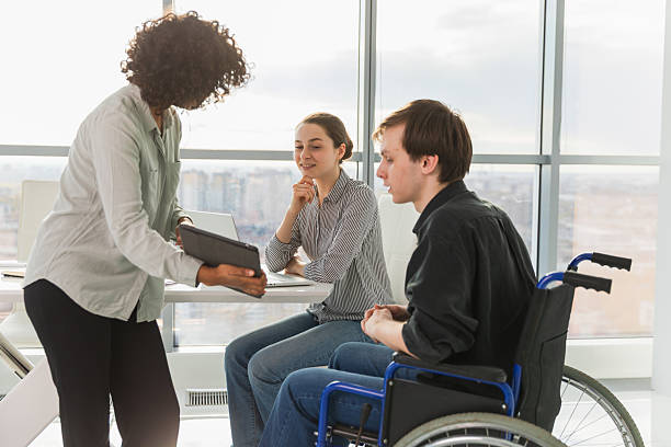 istock Teamwork brainstorm. Diverse multiracial colleagues man in chair for people with disability working together. Group of people sitting in creative office discussing business. Young professional team. 2248711447