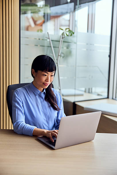 istock Asian Woman Working on Laptop at Modern Office Desk in Bright Workspace 2248720314