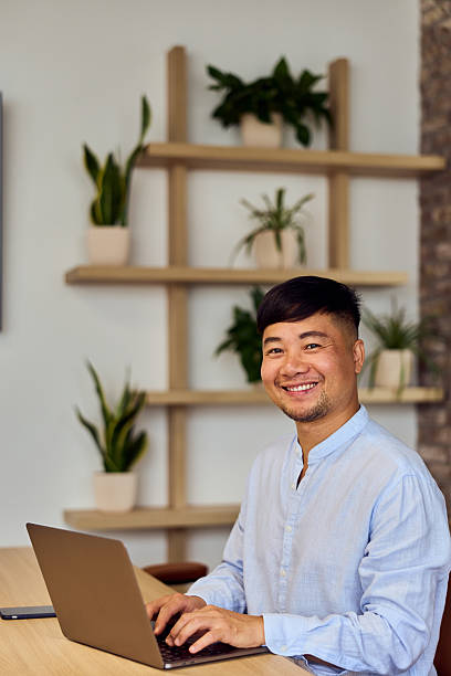 istock Asian Professional Working at Modern Home Office With Laptop, Plants, and Warm Smile 2248720344