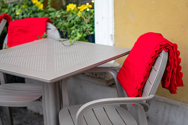istock Plastic garden chairs and table with red blankets draped over backrests positioned beside a yellow building façade outside 2248726986