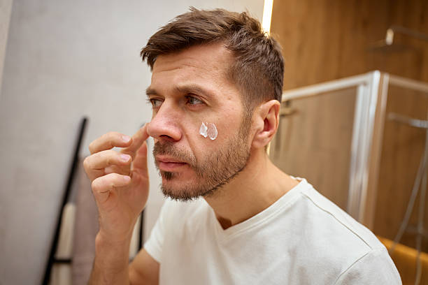 istock Man standing in bathroom and applying face cream to skin 2248730263