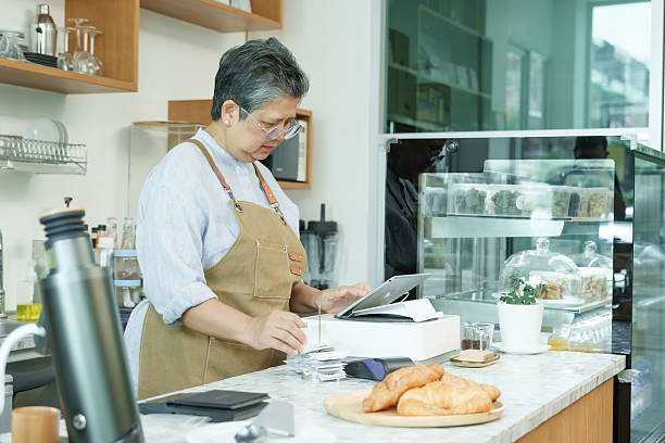 istock Asian senior female cafe owner standing behind counter using tablet handling receipts concentrating on orders working confidently enjoying active post-retirement lifestyle managing business. 2248732357