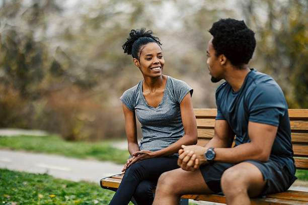 Smiling african american man and woman in activewear having a conversation while sitting on a park bench outdoors