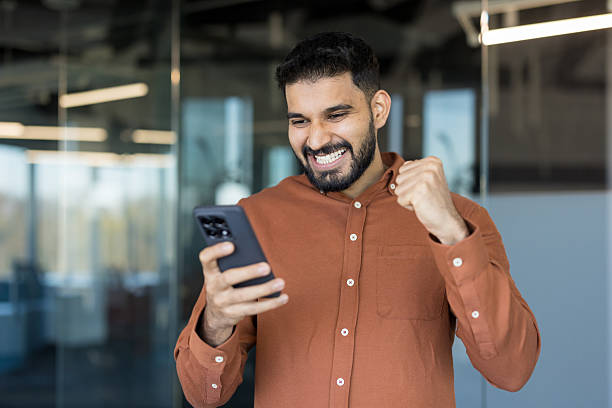 istock Young man celebrating success holding smartphone in office 2248733899