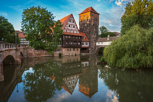 Historic Nuremberg riverside scene featuring a medieval tower, timbered house, and arched bridge reflected in calm water, capturing Bavarian charm and timeless architecture.