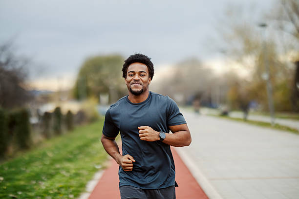 Young african american man jogging on an outdoor track, smiling, staying fit and energetic in an urban park setting during daytime