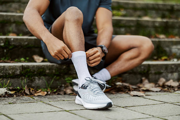Man sitting on concrete stairs putting on white athletic socks getting ready for exercise in an outdoor park setting