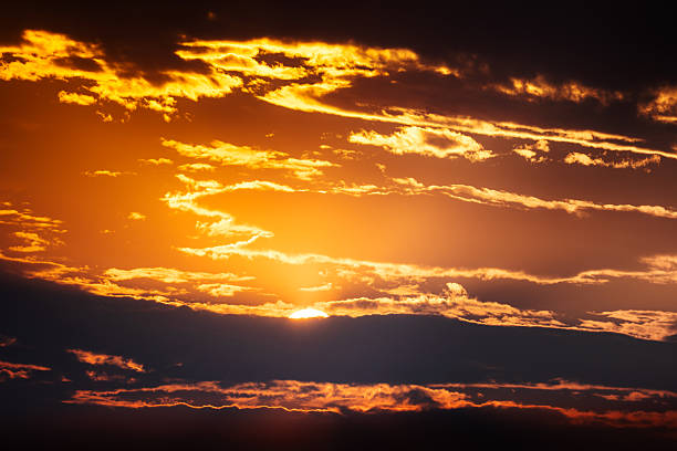 A dramatic sunset scene bathes the sky in golden and orange tones as clouds drift above a dark horizon. This image conveys calm, twilight beauty and the awe of nature's evening light. Botswana, Africa