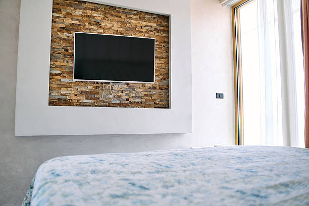 Modern Bedroom Design Featuring a Stylish Wall-Mounted TV with Stone Accent and Cozy Bedding Enhancing the Relaxing Ambiance of the Space