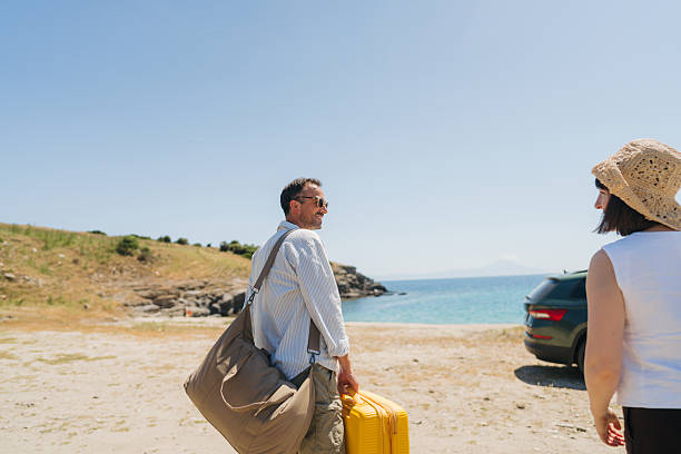 Photo of a happy couple on the summer road trip, unpacking the car with their suitcases and bags