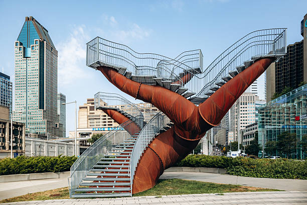 Montreal, Canada  August 14, 2025: A striking public art installation with large rust-colored steel structures and elevated walkways set against the modern downtown skyline of Montreal