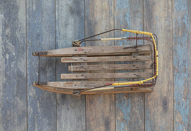 A traditional wooden sled with colorful woven fabric seating rests on a snow-covered path. The sled features a blue pull rope and curved runners, with a forested area faintly visible in the background. \nShot with Canon R5