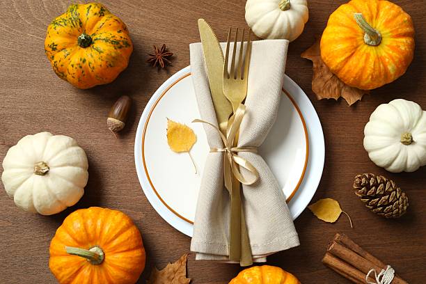 istock Fall-inspired table decor idea. Top view of plate, cutlery, tablecloth, pumpkins, dry leaves, napkin, anise, cinnamon, acorns on pastel brown background with blank space for ad or message 2248763546
