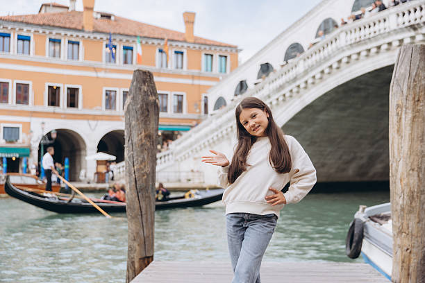 Young girl smiling on a pier with a gondola passing and the iconic Rialto Bridge in the background, Venice travel