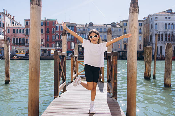 Young girl smiling and spreading arms wide on a wooden dock over the Grand Canal, enjoying summer travel