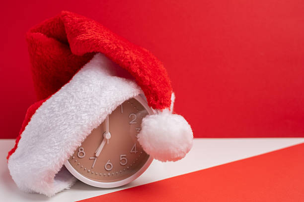 istock Alarm clock covered with santa hat on red and white background. Holiday Countdown. 2248769951