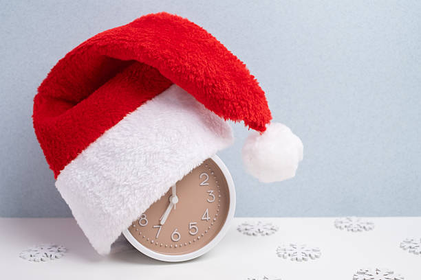 istock Alarm clock covered with santa hat on red and white background. Holiday Countdown. 2248770160