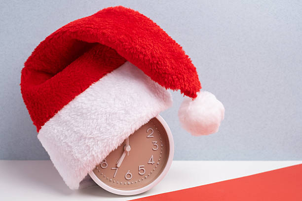 istock Alarm clock covered with santa hat on red and white background. Holiday Countdown. 2248770181