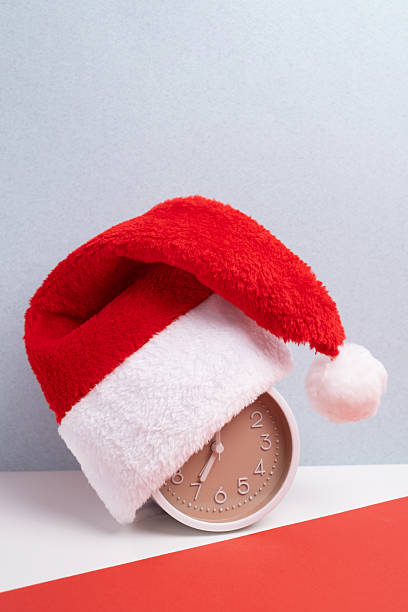 istock Alarm clock covered with santa hat on red and white background. Holiday Countdown. 2248770218