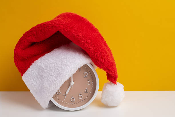 istock Alarm clock covered with santa hat on a yellow background. Holiday Countdown. 2248770995