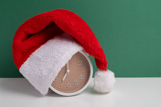 istock Alarm clock covered with santa hat on a green background. Holiday Countdown. 2248771015