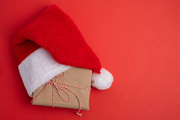 istock Santa hat and kraft-wrapped present on vibrant color background. Minimalist festive gift. 2248771536