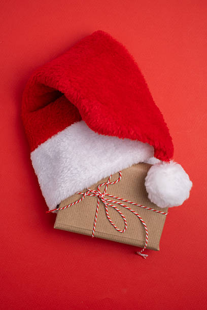 istock Santa hat and kraft-wrapped present on vibrant color background. Minimalist festive gift. 2248771540