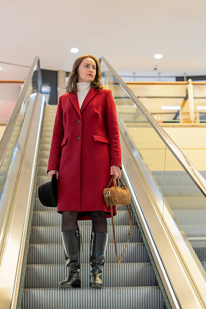 istock Stylish young woman in bright coat standing on escalator steps, creating modern urban lifestyle scene with dynamic city atmosphere 2248771962