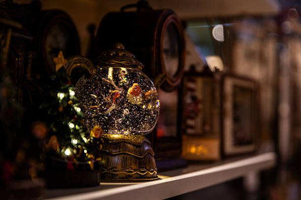 Illuminated snow globe with birds and glitter inside on a shelf, symbolizing winter wonder and cozy decoration for Christmas.
