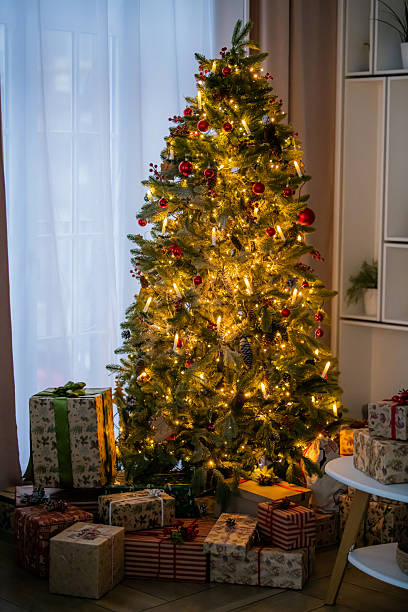 istock Decorated Christmas tree with glowing lights and gift box under it in living room. 2248774617