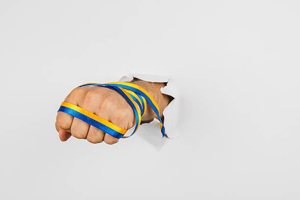 istock Fist breaking through wall with blue and yellow ribbons in bright setting 2248784952