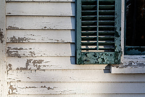 Close-up of a peeling white clapboard wall paired with a weathered green shutter at Ambler Farm in Connecticut, showcasing rustic charm and age.