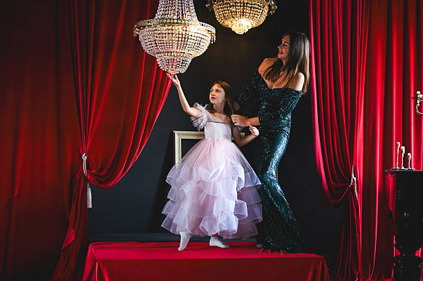 Mother and daughter standing on a red stage with red curtains and sparkling chandeliers