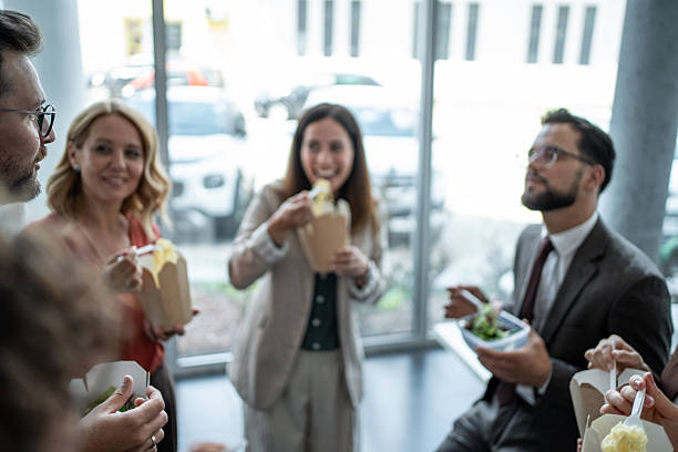 Business colleagues enjoying a relaxed lunch break, talking and eating takeout food in an office setting, fostering team bonding and a positive work environment during their busy day