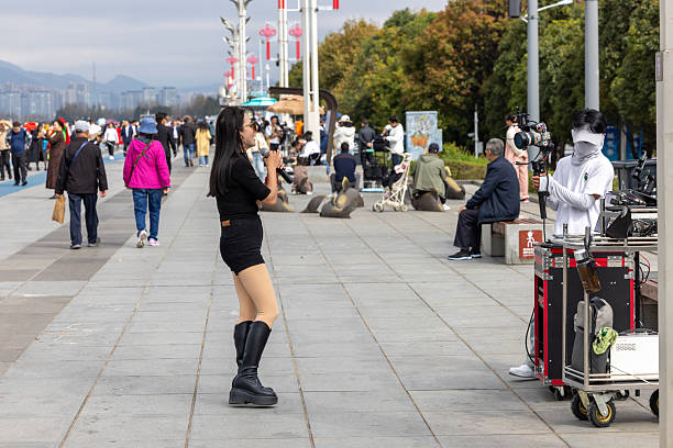 Kunming, China - November 1, 2025: A girl is singing and doing the live streaming at the lake side of Dian lake. Live streaming become a popular new career for earning at China. People are doing different live streaming at different platforms like TikTok, Rednote, Bili Bili etc.