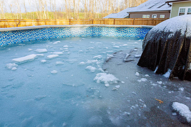 istock Ice covered backyard pool surrounded by trees house during winter 2248800353