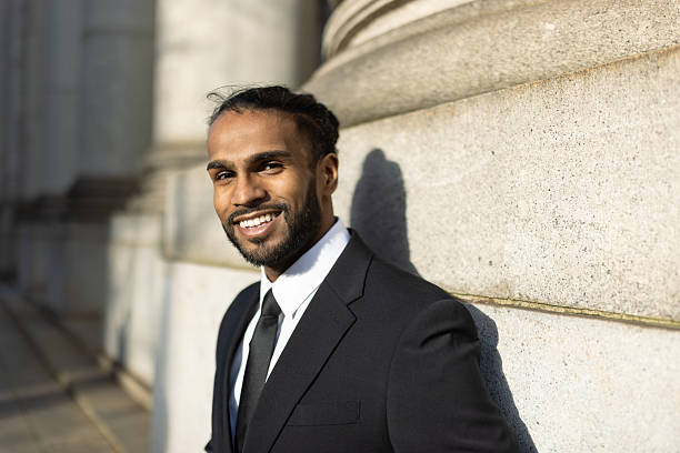 A confident professional poses in a formal suit, leaning against a stone column outdoors. Bright and optimistic mood, perfect for business and lifestyle concepts.