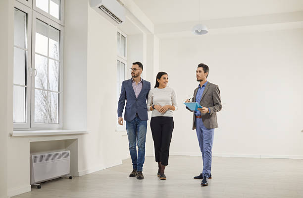 istock Handsome, bearded male real estate agent in suit with documents in his hands advises young, happy couple before buying new apartment. 2248802427
