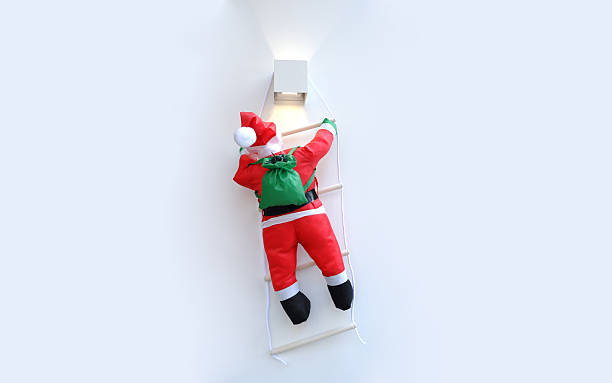 istock Santa Claus decorative doll climbing up a ladder on a white wall, Christmas background image 2248803379