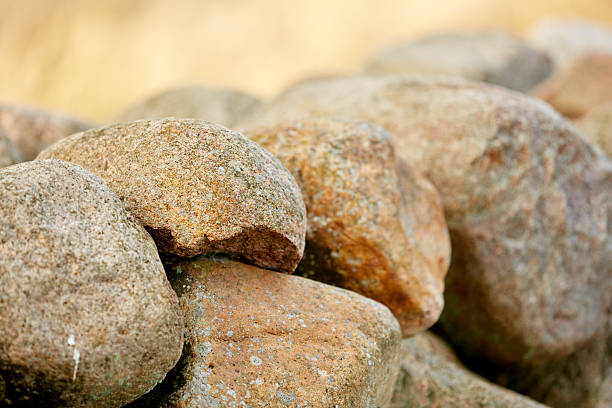 A detailed close-up of weathered granite and pebble stones stacked into a rustic wall. The warm autumn light highlights textures, tones, and natural character, evoking calm Danish countryside scenery and outdoor nature imagery suitable for stock collections.