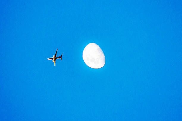 istock An airplane soaring across a clear blue sky with the moon in view 2248813733
