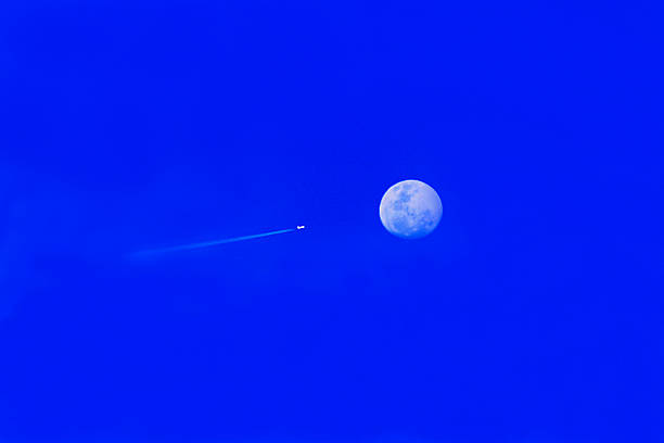 moon and airplane in the blue sky, contrail and haze