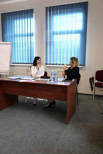 istock Women discuss charts and documents while sitting at a desk in a bright office with water and notebooks. 2248815453