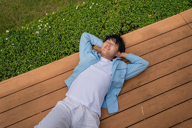 Young asian man resting outdoors on a wooden deck, taking a break.