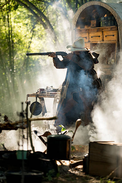 istock A cowboy aiming gun in a forest camp, with sunlight streaming through the smoke 2248815886