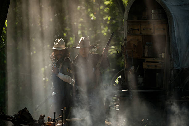istock Two cowboys aiming rifles in a forest camp, with sunlight streaming through the smoke 2248815952
