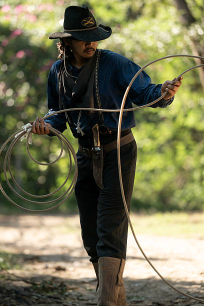 A cowboy handling a lasso rope for training at a rustic camp setup with wooden storage and cooking tools in the background