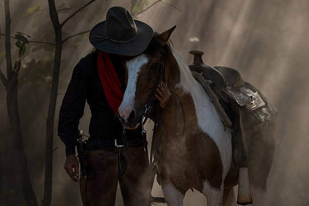 A cowboy leading his saddled horse through a dusty forest as sun rays stream through the trees